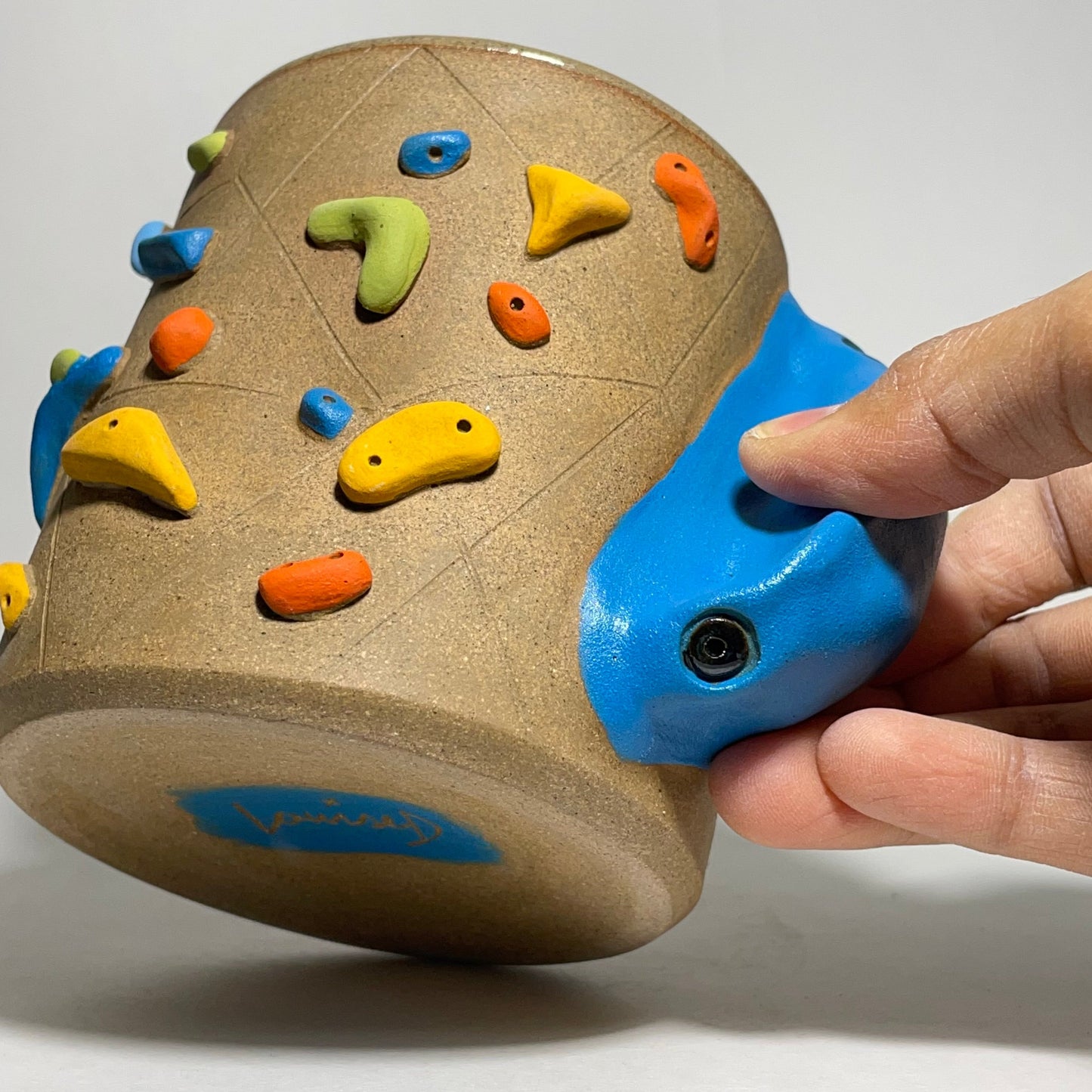 Colorful rock climbing holds on a cylindrical device held by a hand against a white background