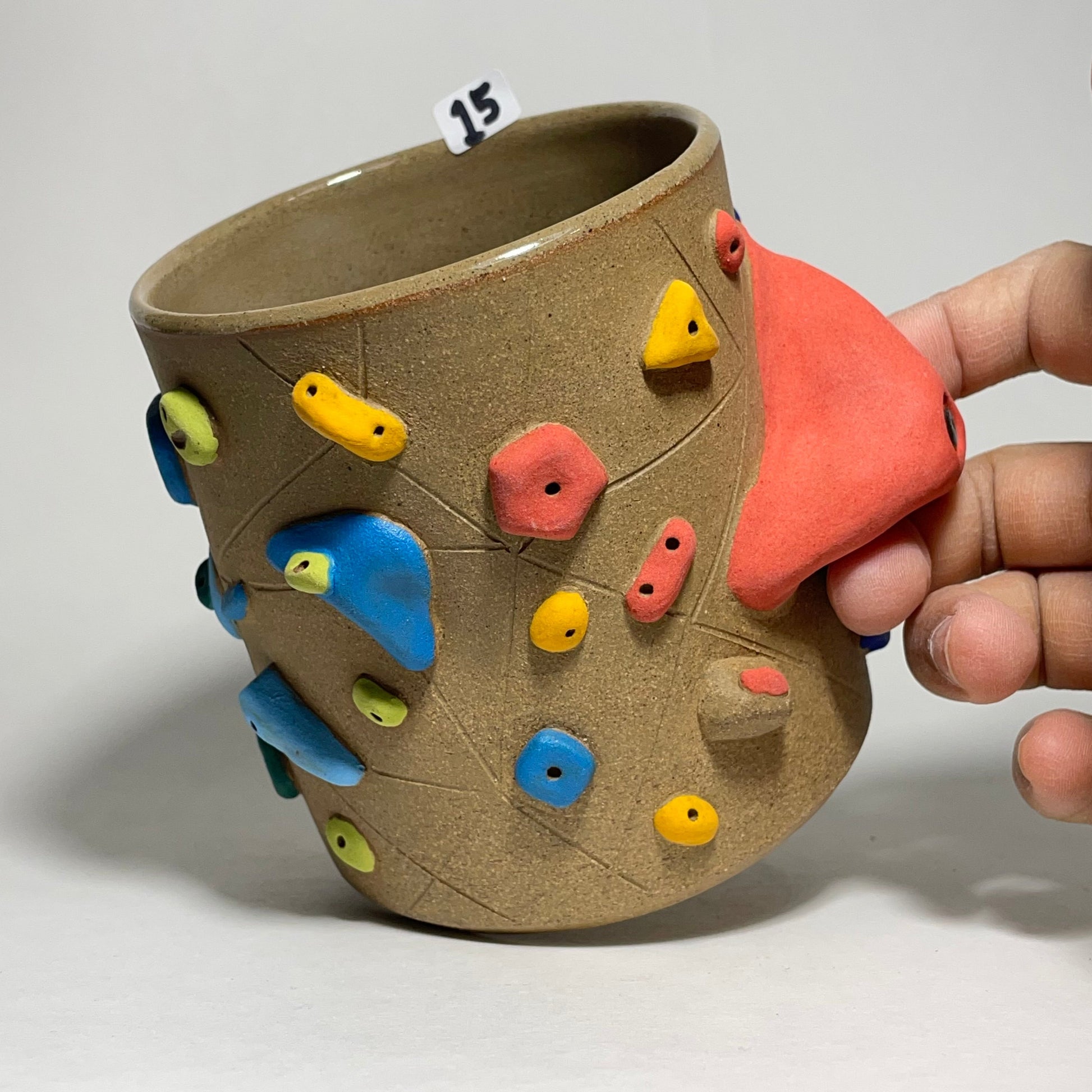 Ceramic cup with colorful climbing holds held by a hand against a white background