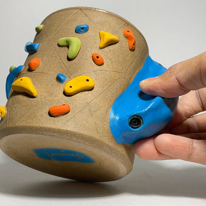 Colorful rock climbing holds on a cylindrical device held by a hand against a white background